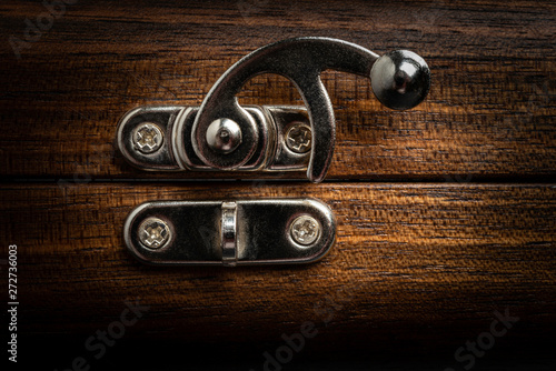 A close-up or macro look of a silver-color metal sliding lock latch in an open position attached to a polished wooden box in horizontal image format.