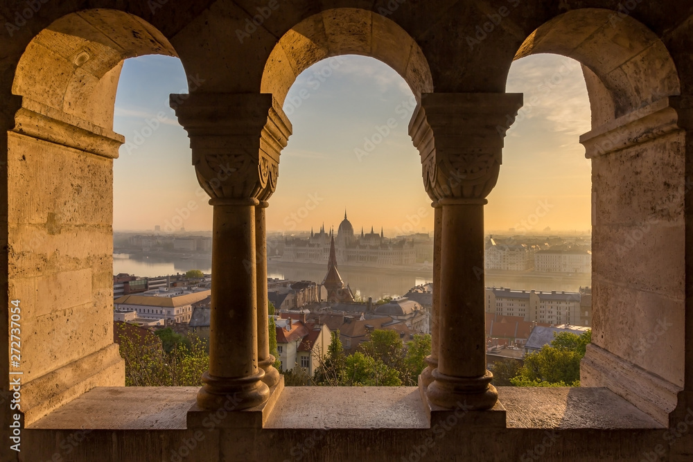 Aerial view of the Parliament of Hungary through Gothic windows of Fisherman's Bastion (Halaszbastya) at sunrise with beautiful sky and clouds , Budapest, Hungary