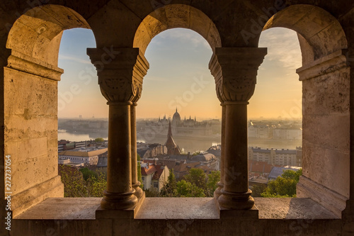 Aerial view of the Parliament of Hungary through Gothic windows of Fisherman s Bastion  Halaszbastya  at sunrise with beautiful sky and clouds   Budapest  Hungary