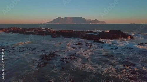 Cinematic wide shot tracking forward over water from drone of Table Mountain from Big Bay, Blouberg on a perfect late afternoon in Cape Town, South Africa. Tilt and jib up passing seagull island.
