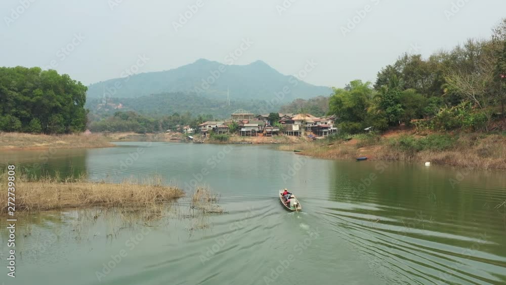 View from above, stunning aerial view of a traditional long tail boat with tourists on board sailing on the Nam Ngum River, Thalat village in the background, Luang Prabang, Laos. View from above, stunning aerial view of a traditional long tail boat with tourists on board sailing on the Nam Ngum River, Thalat village in the background, Luang Prabang, Laos.