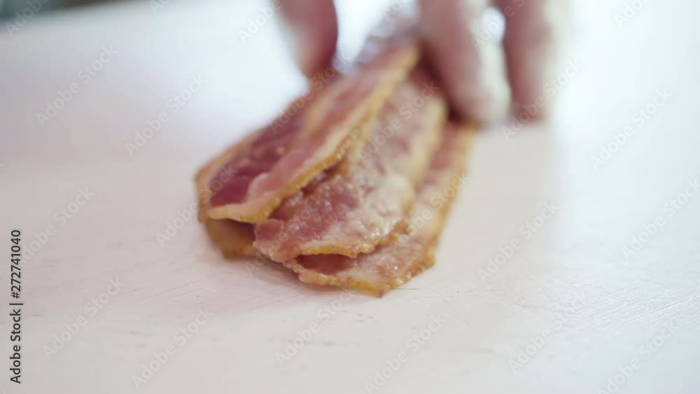 Slicing bacon strips into bacon bits on a white cutting board. Slicing bacon strips into bacon bits on a white cutting board.
