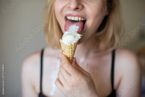 Sexy blonde licks a waffle cone. Ice cream is melting, erotically draining through the body of an attractive woman. Beautiful girl in black underwear smeared with ice cream. Close-up