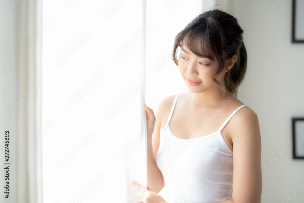 Portrait of beautiful young asian woman standing look at the window and smile while wake up with sunlight at morning, girl happy with fresh and cheerful, lifestyle and relax for wellness concept. Portrait of beautiful young asian woman standing look at the window and smile while wake up with sunlight at morning, girl happy with fresh and cheerful, lifestyle and relax for wellness concept.