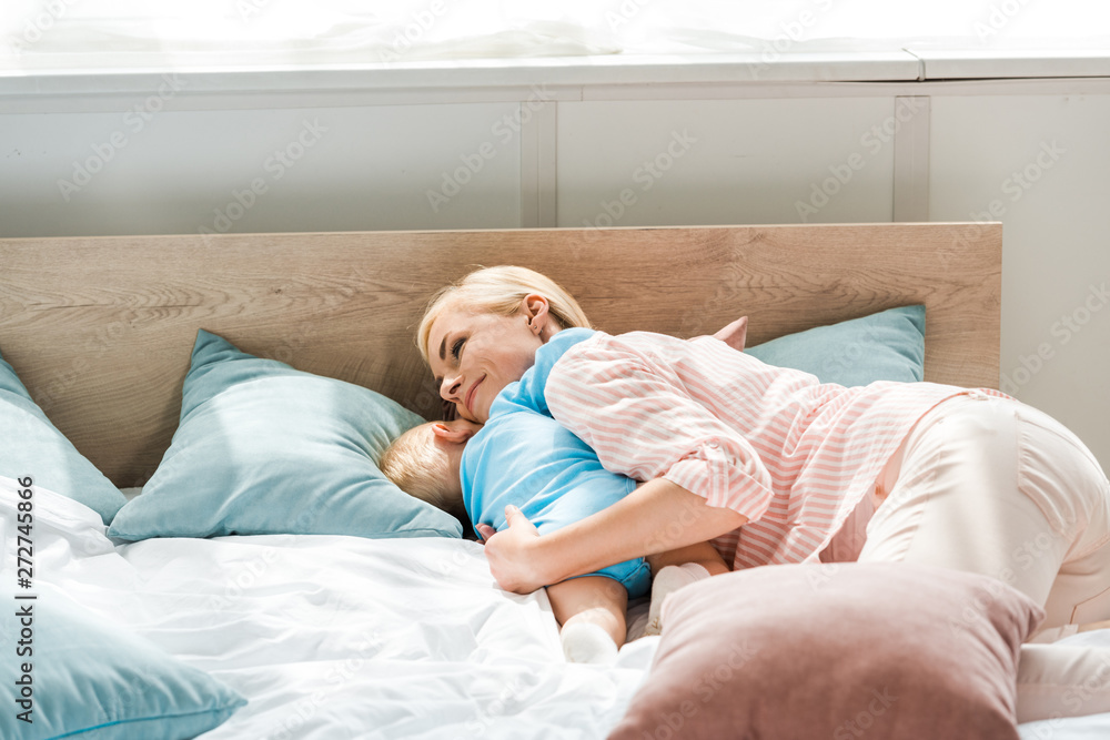 happy mother hugging toddler son while lying on bed and hugging toddler son happy mother hugging toddler son while lying on bed and hugging toddler son