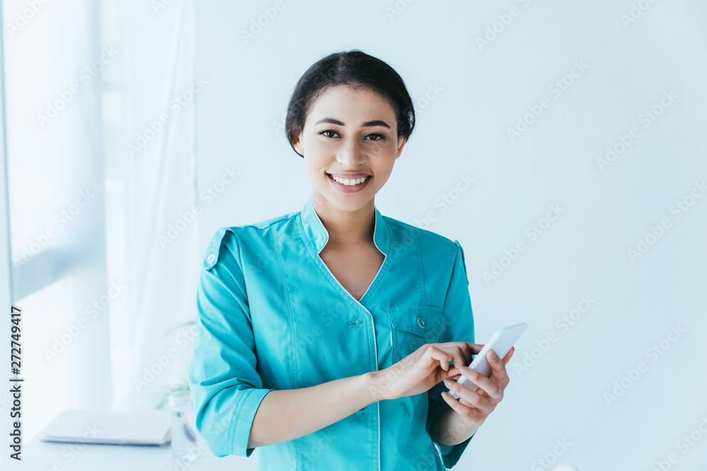 cheerful latin nurse using smartphone and smiling at camera cheerful latin nurse using smartphone and smiling at camera