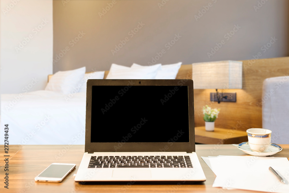 Laptop,smart phone and document on wooden table of defocused white pillow on bed decoration with light lamp in hotel bedroom interior background,Leisure and travel in the holiday concept.