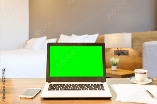 Laptop smart phone and document on wooden table of defocused white pillow on bed decoration with light lamp in hotel bedroom interior background Leisure and travel in the holiday concept.