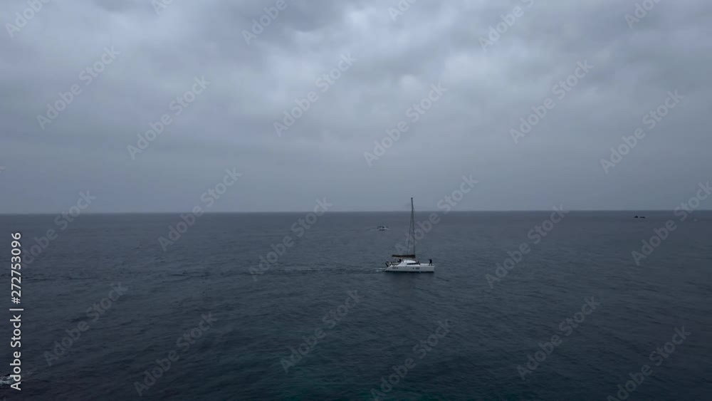 Wide shot of a catamaran in a cloudy red beach in Santorini island Wide shot of a catamaran in a cloudy red beach in Santorini island