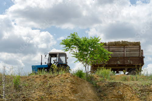 Blue tractor with hay in a trailer rides on the edge of a cliff