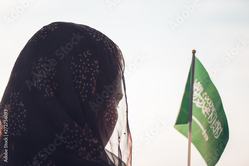 Muslim woman in scarf with Saudi Arabia flag of at sunset.Concept