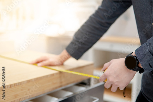 Asian man interior designer using tape measure for measuring size of wooden countertop in modern kitchen showroom in furniture store. Shopping material design for home improvement.