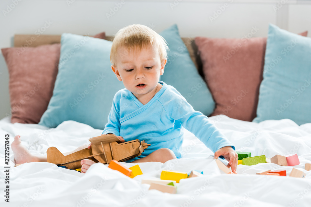 toddler kid playing with wooden biplane near colorful toy blocks on bed toddler kid playing with wooden biplane near colorful toy blocks on bed