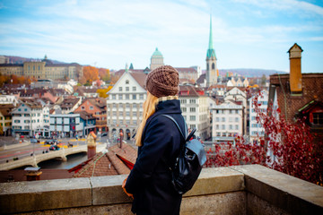 Young blonde tourist girl in warm hat and coat with backpack walking at cold autumn in Europe city enjoying her travel in Zurich Switzerland