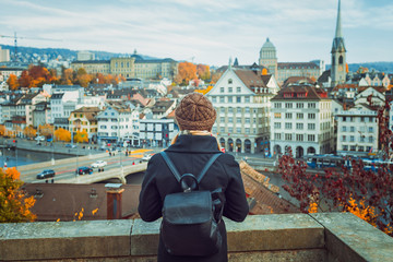 Young blonde tourist girl in warm hat and coat with backpack walking at cold autumn in Europe city enjoying her travel in Zurich Switzerland
