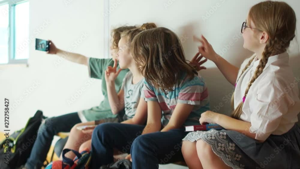 Children with backpacks are sitting on a bench, laughing and talking. Teenagers photographed on the smartphone's camera in the school corridor during the break Children with backpacks are sitting on a bench, laughing and talking. Teenagers photographed on the smartphone's camera in the school corridor during the break