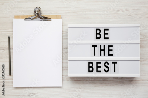 Modern board with 'Be the best' words, clipboard with blank sheet of paper on a white wooden background. Flat lay, overhead, top view, from above. Copy space. photo