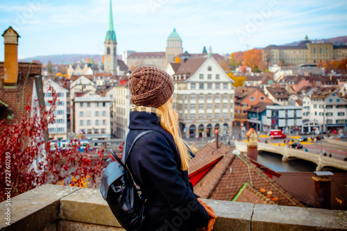 Young beautiful pretty blonde tourist girl in warm hat and coat with backpack walking at cold autumn in Europe city enjoying her travel in Zurich Switzerland © Vasily Makarov