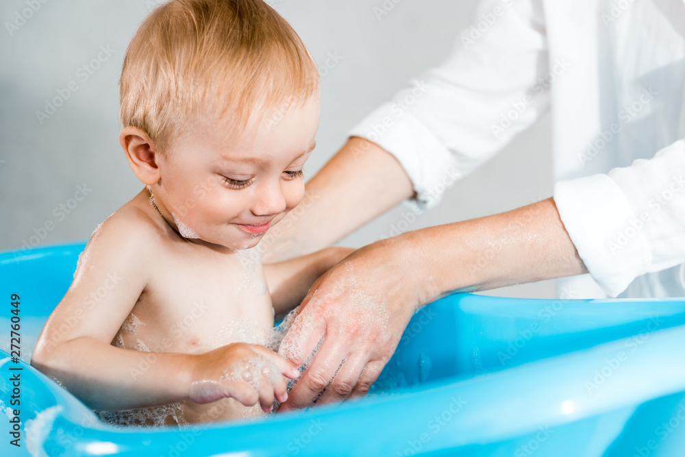 cropped view of woman washing cute toddler kid in baby bathtub cropped view of woman washing cute toddler kid in baby bathtub