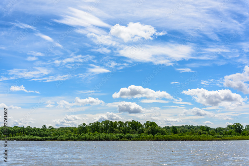 view from the river to the wooded shore. Blue sky with clouds on summer day view from the river to the wooded shore. Blue sky with clouds on summer day