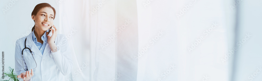 panoramic shot of smiling latin doctor talking by smartphone and looking away panoramic shot of smiling latin doctor talking by smartphone and looking away