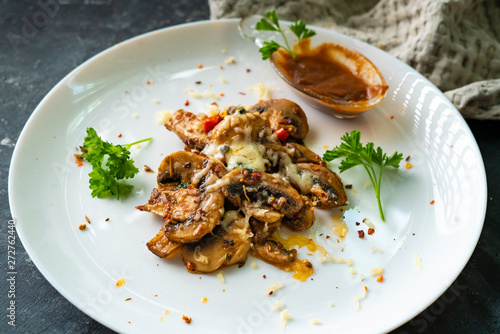 roasted champignons with cheese sauce in a white ceramic plate with herbss photo