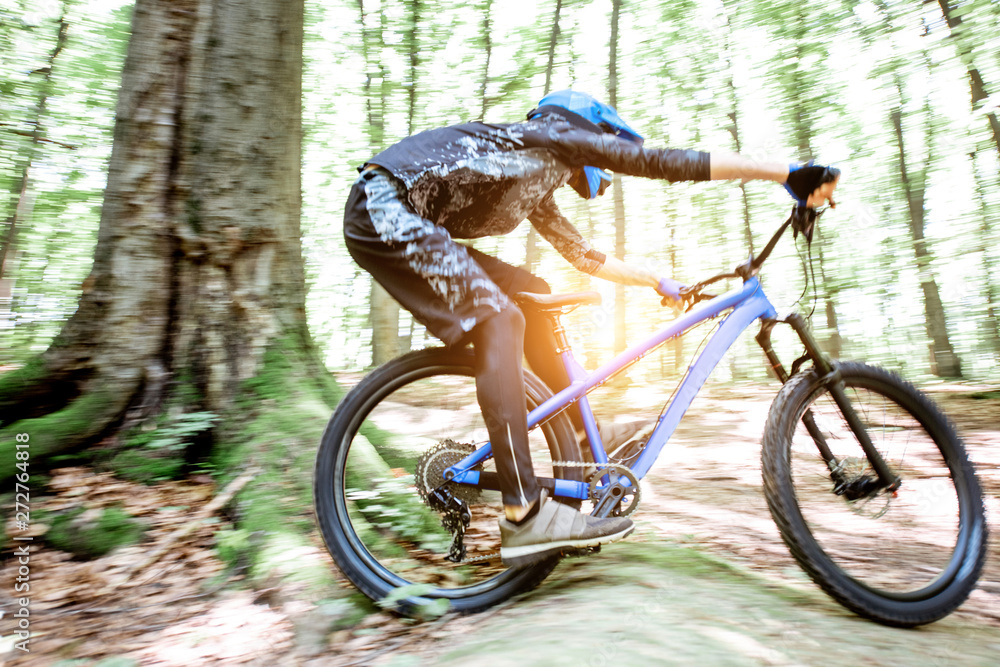 Fototapeta premium Professional well equipped cyclist riding downhill on the off road in the forest. Concept of an extreme sport and enduro cycling. Image with motion blur