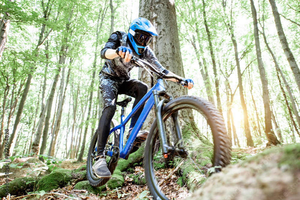 Fototapeta premium Professional well equipped cyclist riding downhill on the off road in the forest. Concept of an extreme sport and enduro cycling