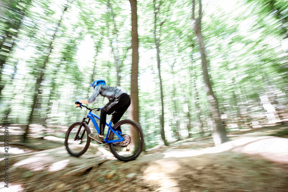 Professional well equipped cyclist riding on the forest track with slides for jumping. Concept of an extreme sport and enduro cycling. Image with motion blur Professional well equipped cyclist riding on the forest track with slides for jumping. Concept of an extreme sport and enduro cycling. Image with motion blur