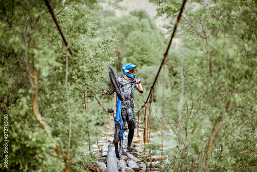 Professional well-equipped cyclist riding on the old wooden bridge in the mountains. Concept of a freeride and off road cycling