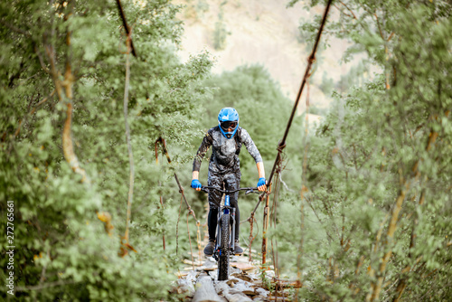 Professional well-equipped cyclist riding on the old wooden bridge in the mountains. Concept of a freeride and off road cycling
