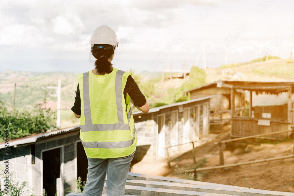 Asian female engineer Put on a white safety hat Wearing a green safety shirt Stand for construction inspection In the construction area