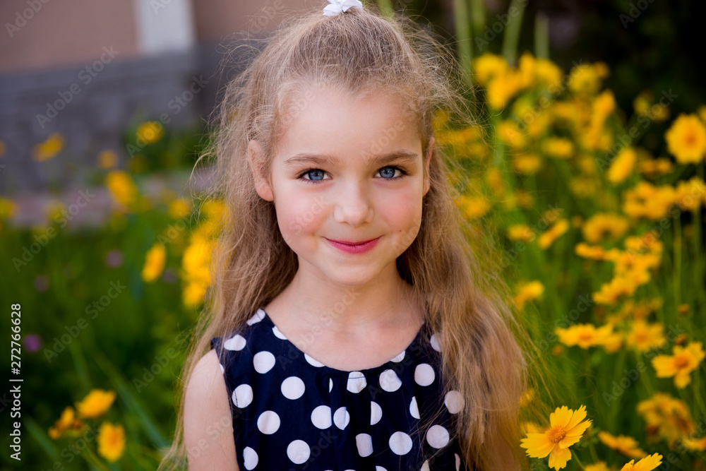 Portrait of a beautiful smiling girl outdoor. Summer portrait of a smiling girl. Little beautiful girl blonde in colors. Garden with yellow flowers, summer girl Portrait of a beautiful smiling girl outdoor. Summer portrait of a smiling girl. Little beautiful girl blonde in colors. Garden with yellow flowers, summer girl