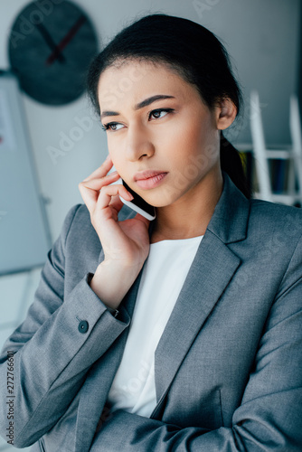 serious latin businesswoman talking on smartphone while looking away in office