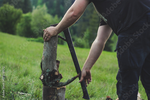 The guy is cutting an old tree in the mountains with an ax. Ukrainian Carpathian Mountains. Bonfire. Tourism. Ax © Yaroslav