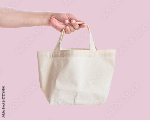 Tote bag canvas white cotton fabric cloth for eco shoulder shopping sack mockup blank template isolated on pastel pink background (clipping path) with woman’s hand handling handle straps