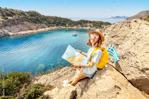 Girl tourist student with map and greek flag standing on top of the hill at background of the inspirational blue lagoon bay. Solo Travel in Greece concept photo