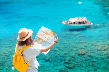Cheerful girl with a map exploring interesting places to travel by ferry or rented boat or yacht in the azure Gulf of the Mediterranean sea