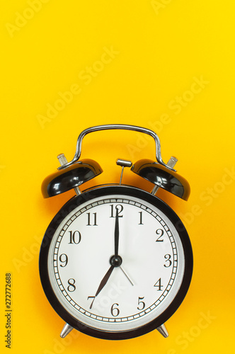 Black retro alarm clock on yellow background top view Flat lay copy space. Minimalistic background, concept of time, deadline, time to work, morning