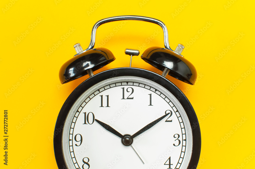 Black retro alarm clock on yellow background top view Flat lay copy space. Minimalistic background, concept of time, deadline, time to work, morning