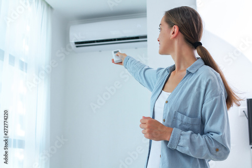 Young woman adjusts the temperature of the air conditioner using the remote control in room at home photo