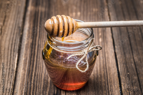 Glass jar of honey and wooden stick with dripping honey on rustic wooden background