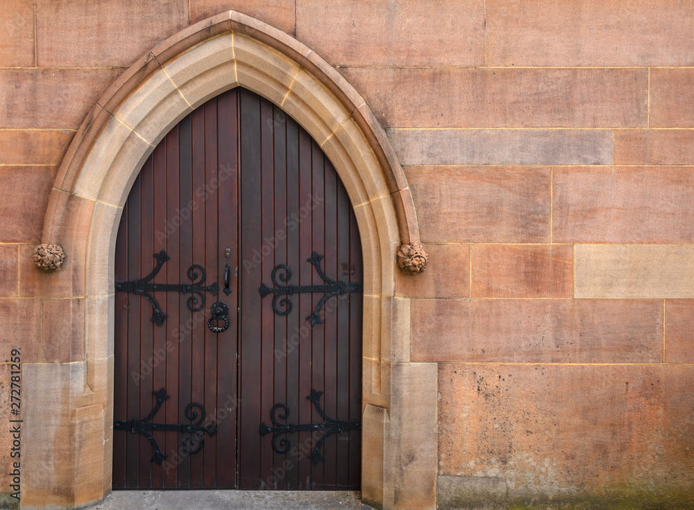 Church entrance door with wrought iron recessed into a colourful textured sandstone pointed archway Church entrance door with wrought iron recessed into a colourful textured sandstone pointed archway