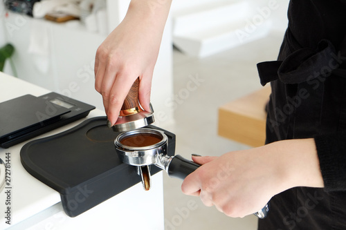 Close up shot of female barista wearing black stylish apron using portafilter coffee machine equipment to press grounded beans near coffee machine in cafe place. Close up, copy space, background. © Evrymmnt