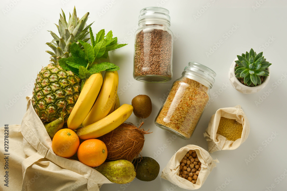 Zero waste and plastic free concept. Grocery shopping eco bag with fruits and cereals in glass jars, white background. Flat lay, top view. Copy space. Zero waste and plastic free concept. Grocery shopping eco bag with fruits and cereals in glass jars, white background. Flat lay, top view. Copy space.