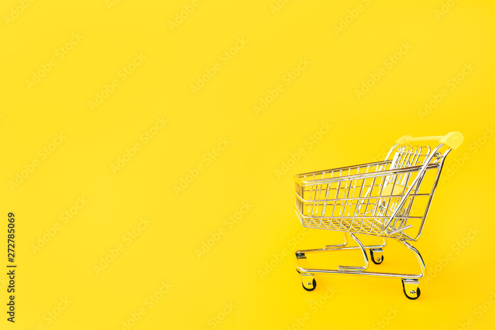 Toy cart for products on a yellow background. Place for text. View from above. The concept of shopping and consumption Toy cart for products on a yellow background. Place for text. View from above. The concept of shopping and consumption