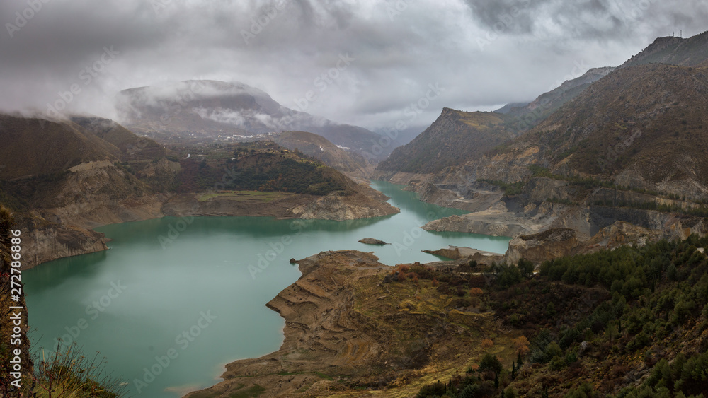 A reservoir in winter in the wild rugged mountains of the Spanish Sierra Nevada near the city of Granada. The clouds are floating low.