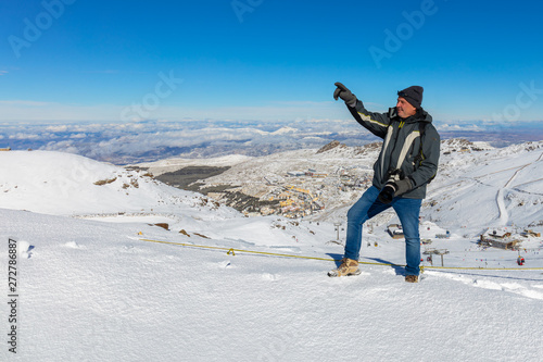 About the place Pradollano. A photographer with a camera points his hand towards the summit. The mountains Spanish Sierra Navada near the city of Granada covered in winter snow. photo