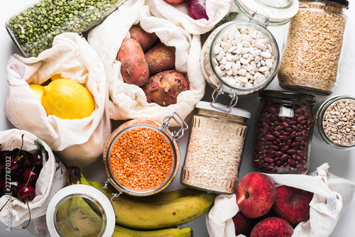 Variety of groceries in glass jars and reusable cotton bags, top view. Zero waste lifestyle concept
