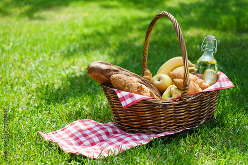 Wicker picnic basket with food and drink in a park.